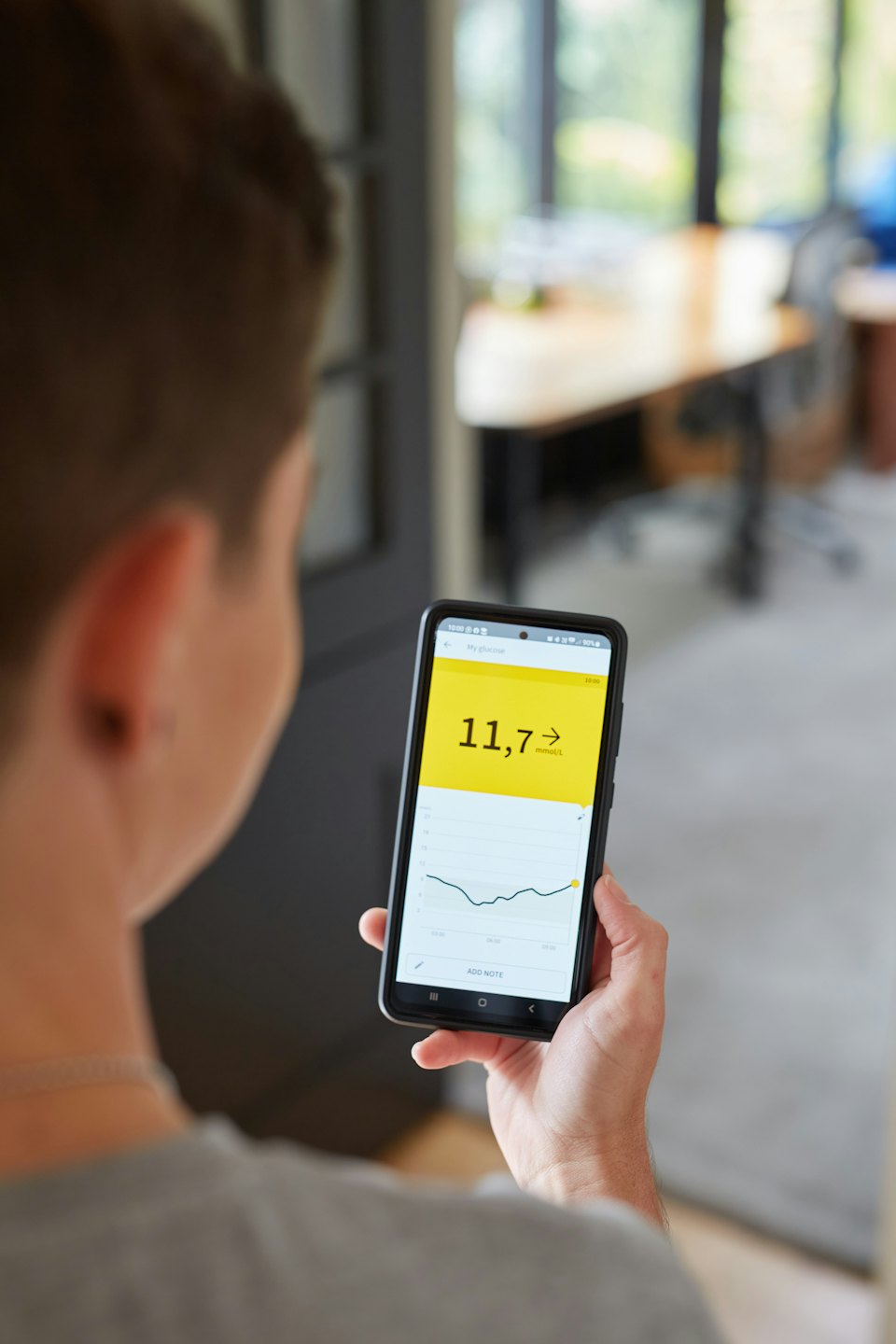 Person checks blood glucose app on smartphone in office.
